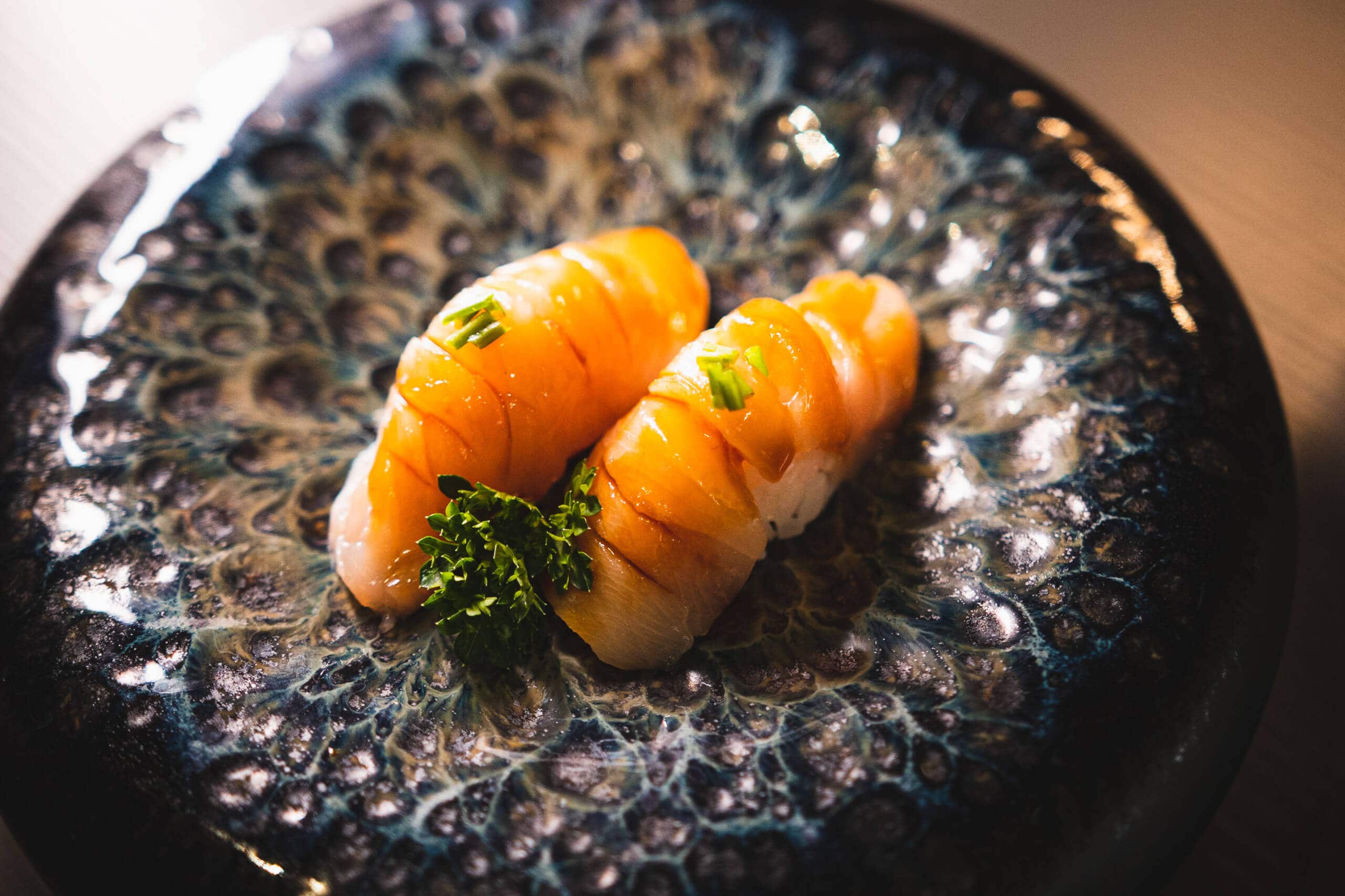 Due pezzi di sushi con pesce fresco e guarnizione di erba cipollina su piatto nero.