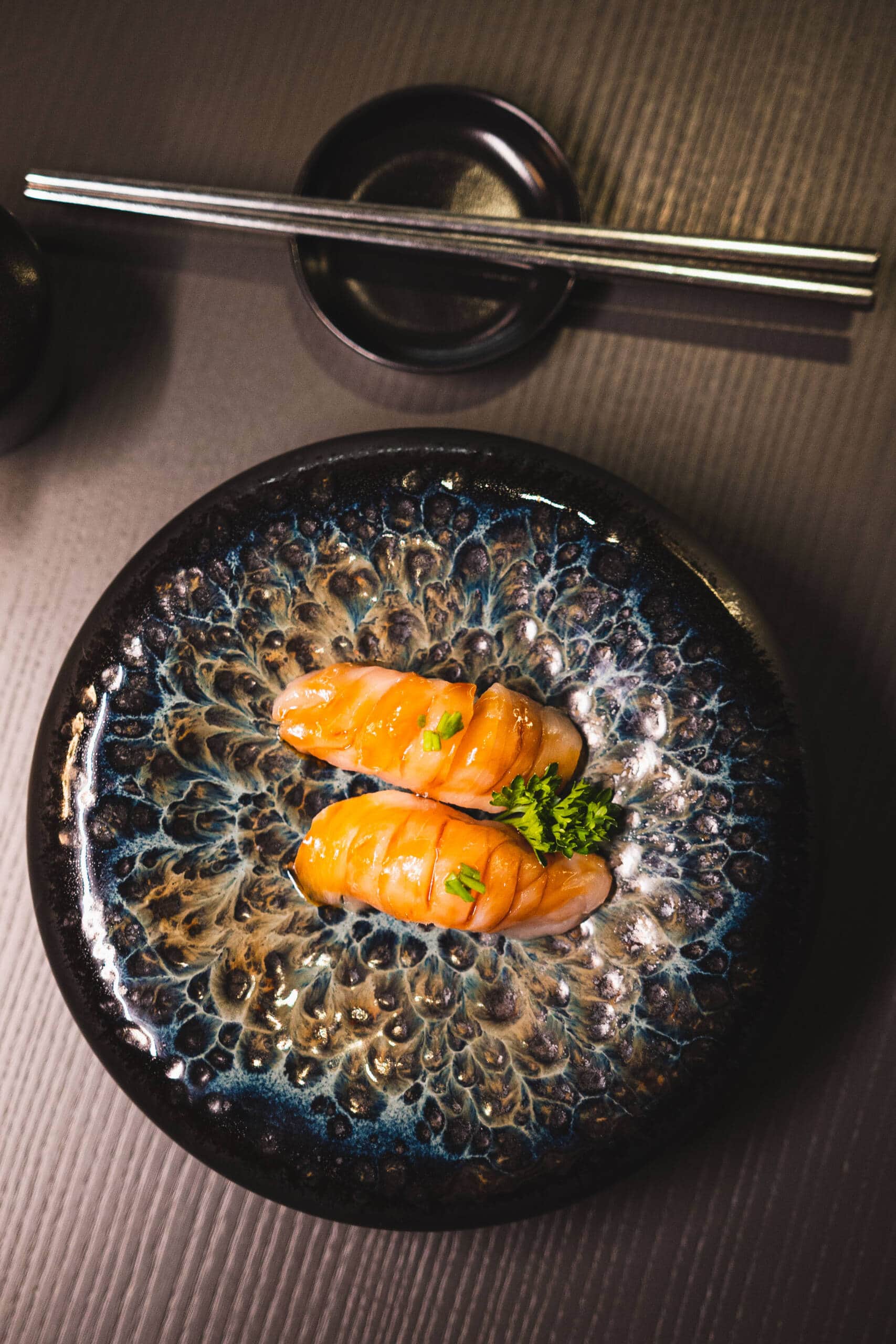 Sushi con salmone fresco e decorazione di erba su piatto nero.