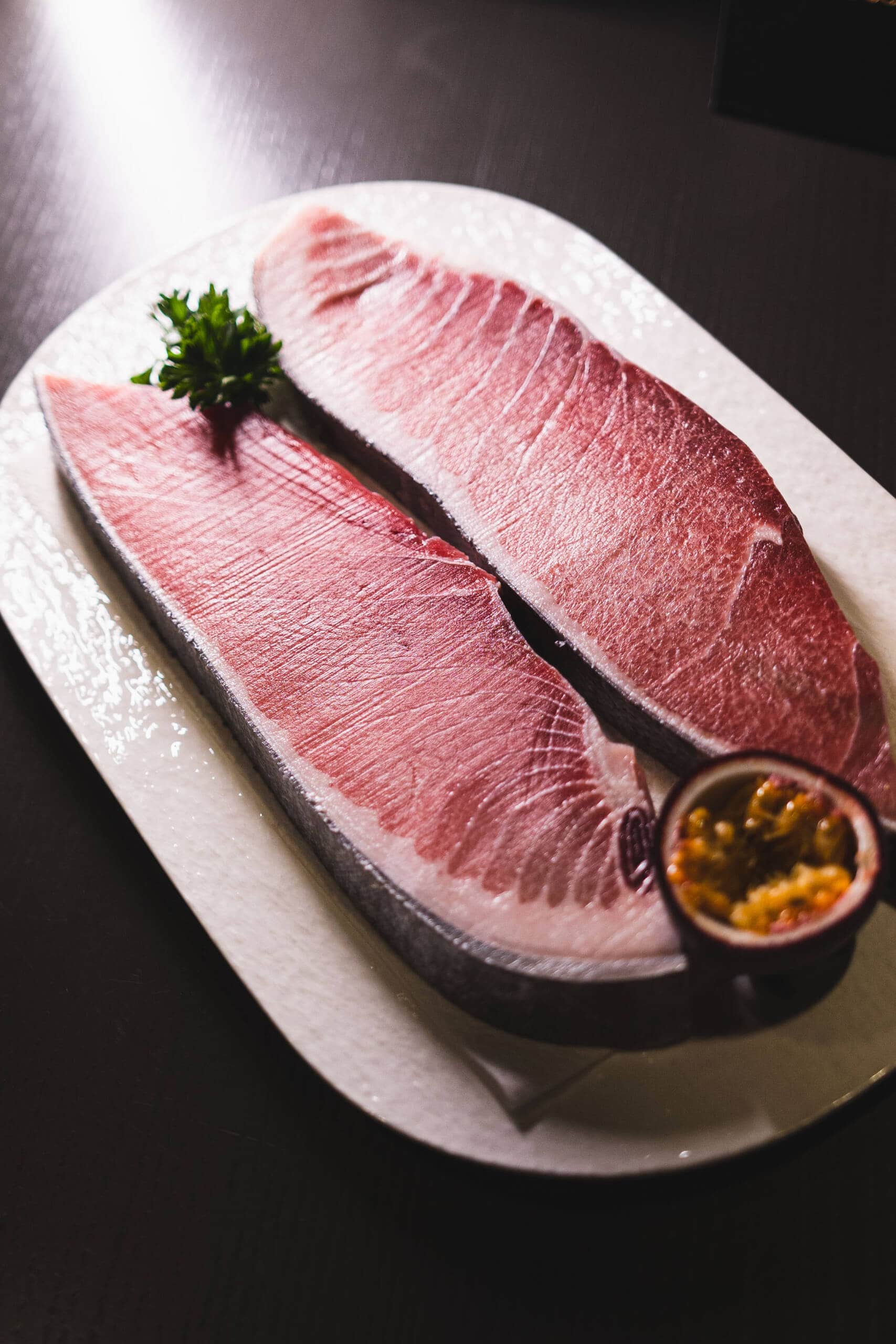 Filetto di tonno crudo su piatto elegante con limone e prezzemolo.