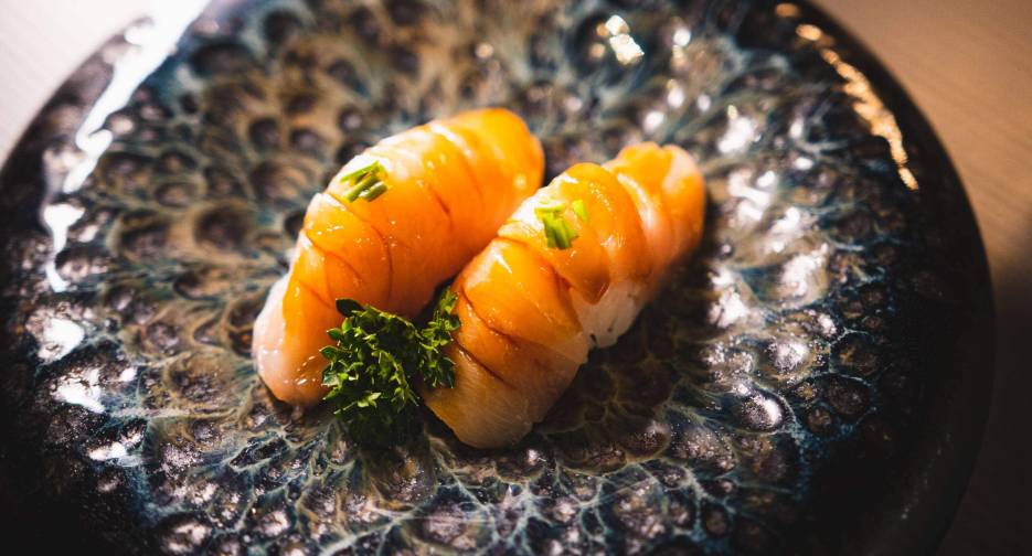 Due pezzi di sushi con pesce fresco e guarnizione di erba cipollina su piatto nero.